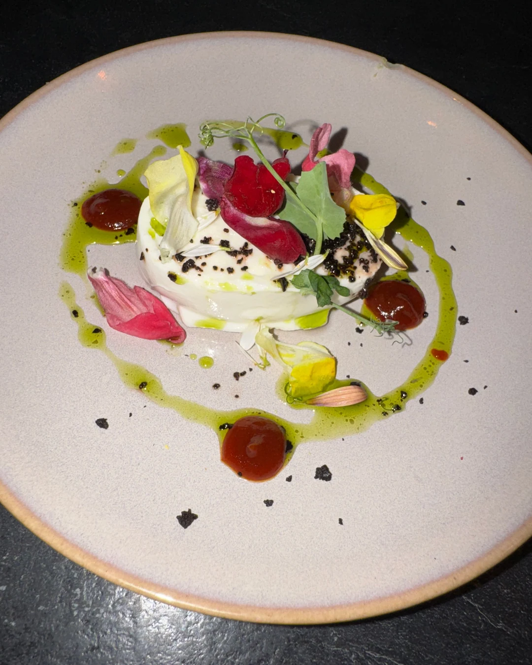Assiette dressée sur une ardoise : fleurs comestibles, pousses, points de coulis et huile verte
