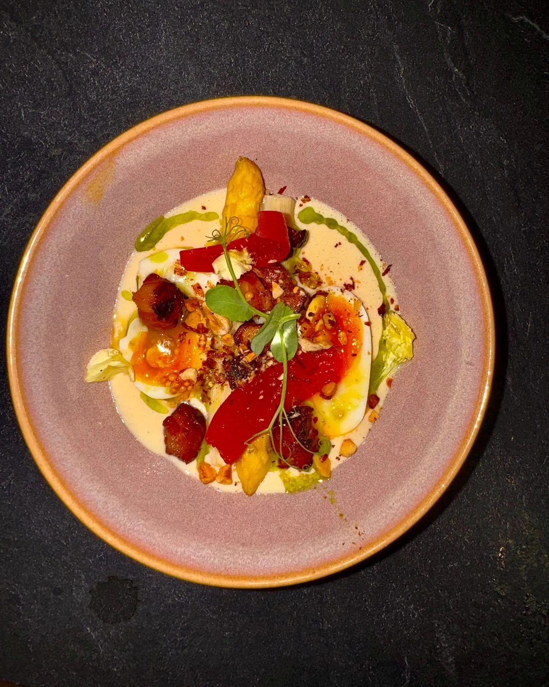 Assiette creuse rose posée sur une ardoise, dressage coloré vu de dessus, pousse au centre