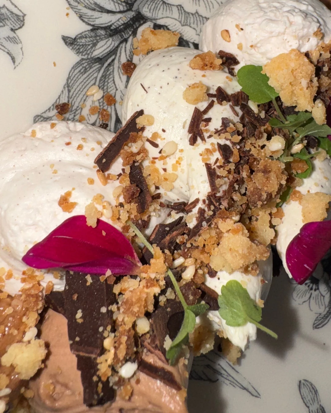 Détail d’un dessert dressé : quenelles, éclats croustillants, pétales et jeunes pousses